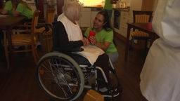 Schülerin redet mit einer älteren Bewohnerin des Pflegeheims, die im Rollstuhl sitzt.