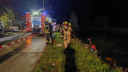 Feuerwehrleute stehen an einem Abhang und halten Seile, im Hintergrund ein Einsatzwagen.