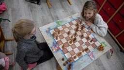 Zwei Mädchen spielen Schach an enem Brett, dass mit Drachen und Rittern verziert ist.
