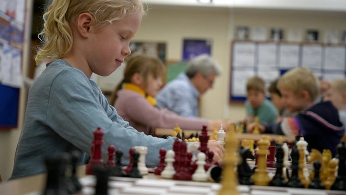 Ein Mädchen sitzt vor einem Schachbrett voller Figuren.
