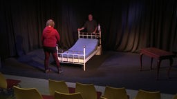 Ein Bett wird auf die Bühne getragen