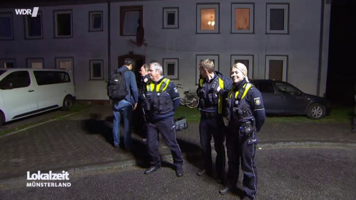 Drei Polizisten vor einem Mietshaus in Gronau mit Wohnungen für Leiharbeiter der niederländischen Fleischindustrie.