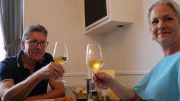 Zwei Personen trinken bei Tisch ein Glas Weißwein.