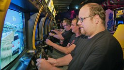 Besucher der Gamescom spielen an alten Spieleautomaten. 