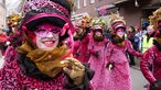 Maskierte Frauen in schwarz-pinkem Kostümen und Hüten laufen beim Rosenmontagsumzug in Münster. 