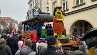 Ein Karnevalswagen mit Fred Feuerstein als Figur fährt neben der Menschenmenge