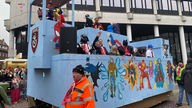 Karnevalisten und Karnevalistinnen auf einem blauem, mit Superhelden bemalter Karnevelswagen in Rheine.