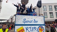 Karnevalisten und Karnevalistinnen auf dem Wagen des "Senats der KUR" auf dem Rosenmontagsumzug in Rheine.