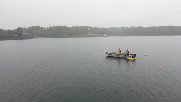 Zu sehen ist der Moehnesee, es ist sehr vernebelt. Auf dem See befindet sich ein Boot.