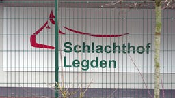 Das Logo des Schlachthofs in Ledgen hinter einem Gitterzaun. 