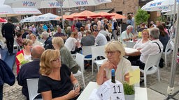 Besucher sitzen an Tischen auf dem Schlemmermarkt