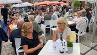 Besucher sitzen an Tischen auf dem Schlemmermarkt