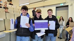Drei der teilnehmenden Schüler halten ihre Urkunden in die Kamera
