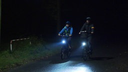 Das Bild zeigt eine Schülerin im Dunkeln auf dem Fahrrad mit einer Begleitperson.