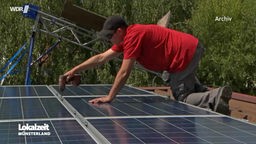 Ein Mann ist auf einem Dach und montiert Solarpanele.