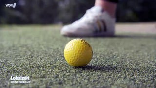 Ein gelber Golfball liegt auf einem Kunstrasen. 