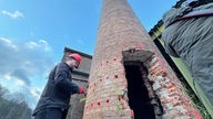 Ein Arbeiter bereitet den Schornstein in Plettenberg für die Sprengung vor. Dazu bohrt er meherere Löcher in die Stein-Oberfläche