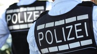 Zwei Polizei-Schutzwesten mit der Aufschrift Polizei von hinten. 