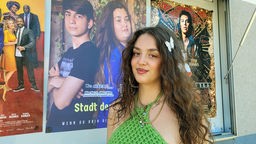 Yagut Janzen, die Sängerin aus dem Film: Stadt der Hoffnung, steht vor dem Kinoplakat des Filmes. 
