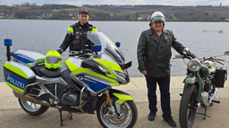 Ein Polizist steht neben einem Motorrad, daneben ist ein zweiter Mann mit Motorrad