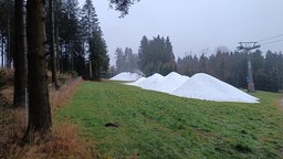 Auf dem Foto ist ein Skihang zu sehen, der noch nicht von Schnee bedeckt ist, außer von einigen Hügeln aus Kunstschnee