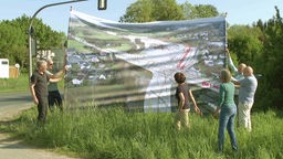 Menschen halten ein Banner hoch, auf welchem die geplante Kreuzung zu sehen ist