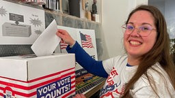 Eine junge Frau steckt einen Stimmzettel in den Schlitz einer Wahlurne
