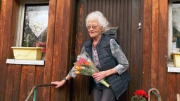 Eine ältere Frau mit Blumen in der hand steht vor einer Tür