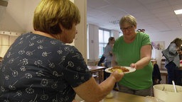 Eine Mitarbeiterin der Essensausgabe für Wohnungslose reicht einer Frau einen Teller mit Spaghetti