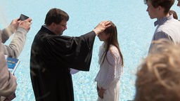 Ein Pfarrer tauft ein Kind im Wasser