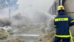 Ein THW-Mitarbeiter schießt Löschwasser auf dampfendes Heu in einer zerstörten Scheune