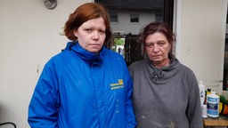 Zwei Frauen in Nahaufnahme vor einem Haus stehend welches von einem Unwetter getroffen wurde. 