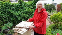Eine ältere Damen in roter Jacke im Garten stehend mit Holzteilen in der Hand vom Unwetter. 