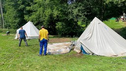 Männer auf einer Wiese bauen Zelte ab