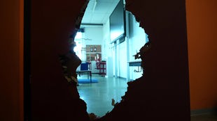 Durch ein Loch in einer Tür ist ein Klassenzimmer zu sehen.