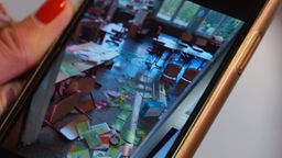 Auf einem Handybildschrim ist das Bild eines verwüsteten Klassenzimmers zu sehen.