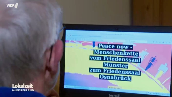 Ein Mann mit weißen Haaren schaut auf einen Laptop, auf dessen Bildschirm "Peace now - Menschenkette vom Friedenssaal Münster zum Friedenssaal Osnabrück" steht. 
