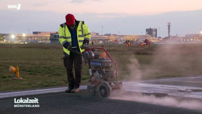 Ein Bauarbeiter am Flughafen Münster Osnabrück bearbeitet frischen Asphalt mit einem Presslufthammer. 
