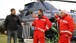 Drei Männer vor einem Hubschrauber.