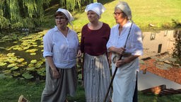 Drei mittelalterlich gekleidete Frauen stehen vor einem Teich