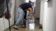 Mann in Badelatschen und Wischmob in überflutetem Flur.