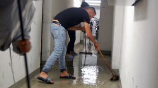 Mann in Badelatschen und Wischmob in überflutetem Flur.
