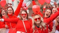 Frauen in roten Kostümen mit Herzmustern.