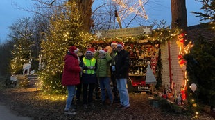 5 Menschen stehen vor dem Stand des kleinsten Weihnachtsmarktes