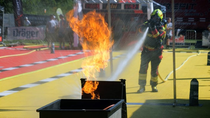Mensch in Feuerwehrmontur löscht mit Wasserstrahl ein Feuer.