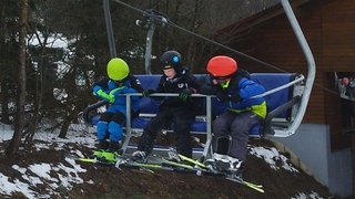 Drei Kinder in Skimontur einem Sessellift