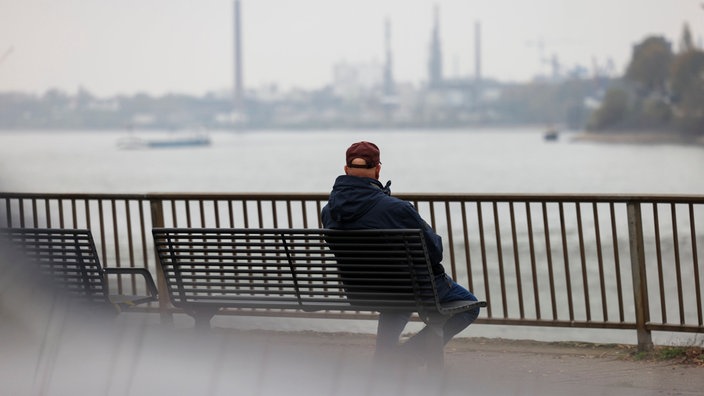 Ein Mann sitzt auf einer Bank und guckt auf den Rhein