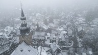 Der Kirchturm einer Kirche in Remscheid-Lüttringhausen und die Dächer im Ort vom Schnee bedeckt. 