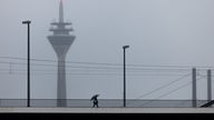 Eine Person mit Regenschirm geht bei Regen über die Oberkasseler Brücke. Im Hintergrund ist der Rheinturm zu sehen.