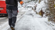 Streusalz wird von einem Mitarbeiter vom Winterdienst auf einen Gehweg gestreut